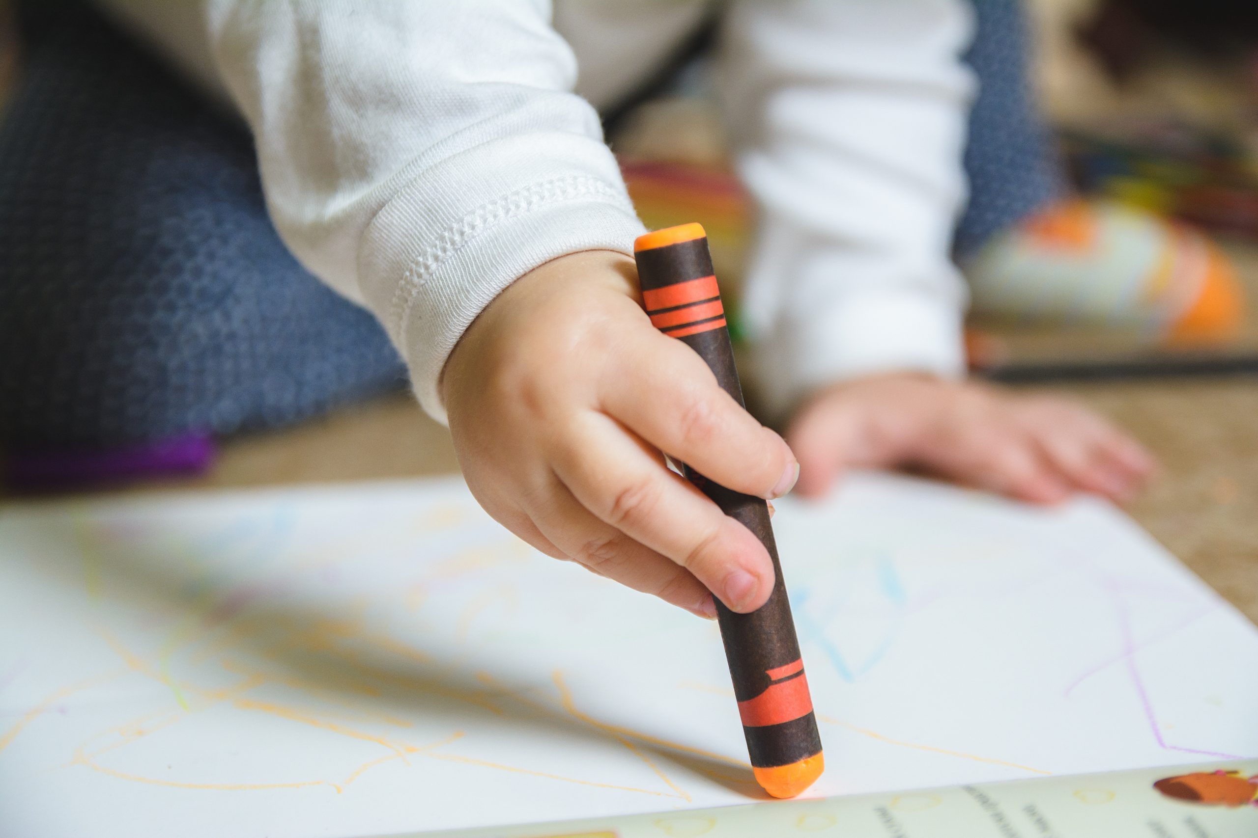 A baby drawing with an orange crayon on the paper